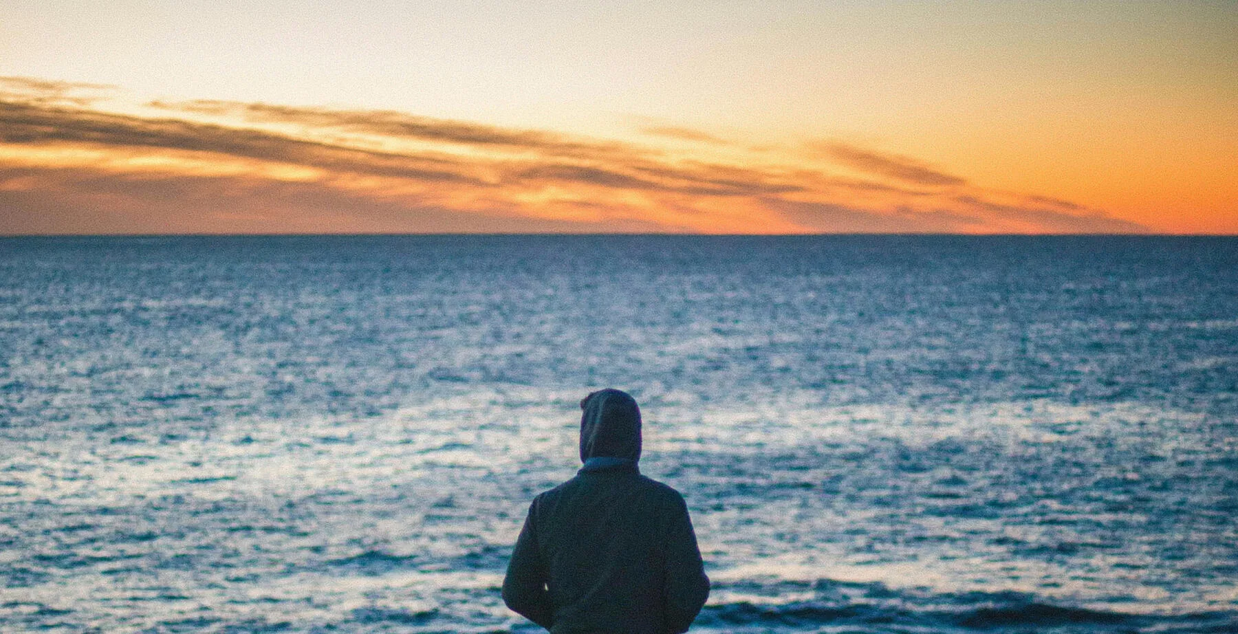 Une personne face à l'océan au coucher du soleil.